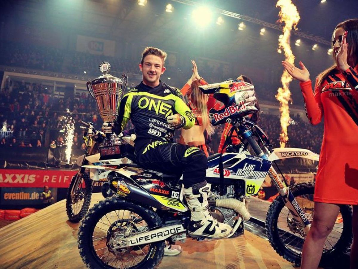 Mann auf Motorrad hält Siegerpokal